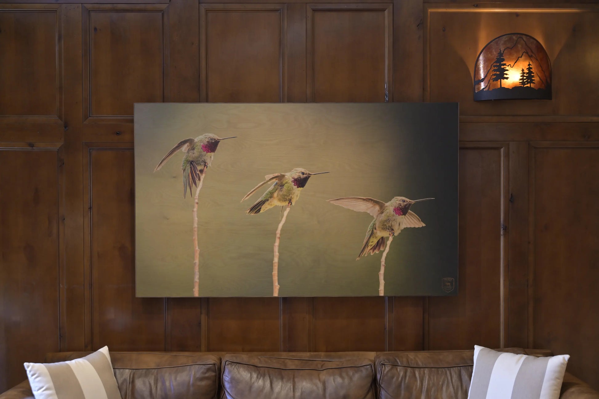 Artistic depiction of three hummingbirds on a wooden wall above a sofa.