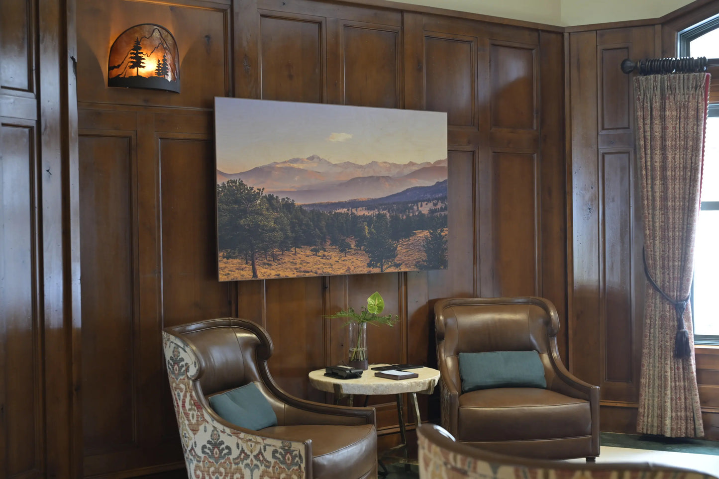 Cozy room with wooden paneling, leather chairs, and a scenic painting on the wall.
