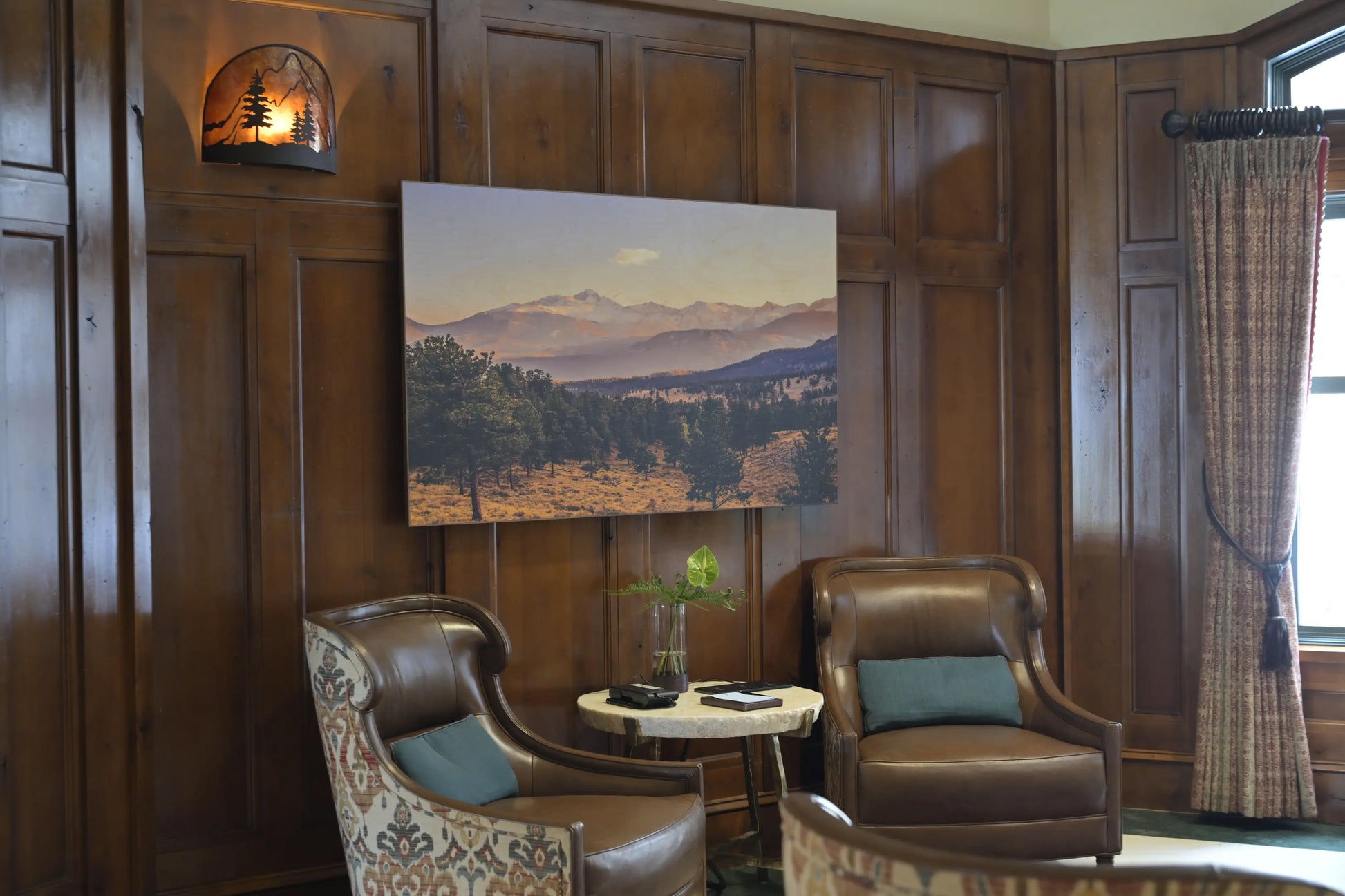 Cozy room with wooden paneling, leather chairs, and a scenic painting on the wall.