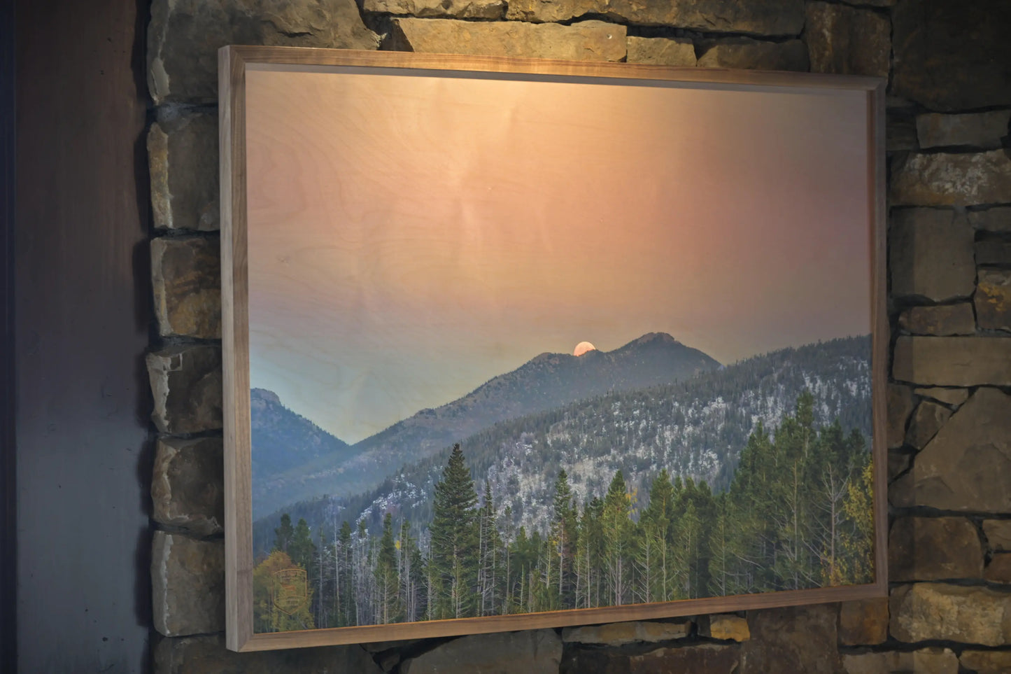 Framed photograph of a mountain landscape with a sunset over a forest.