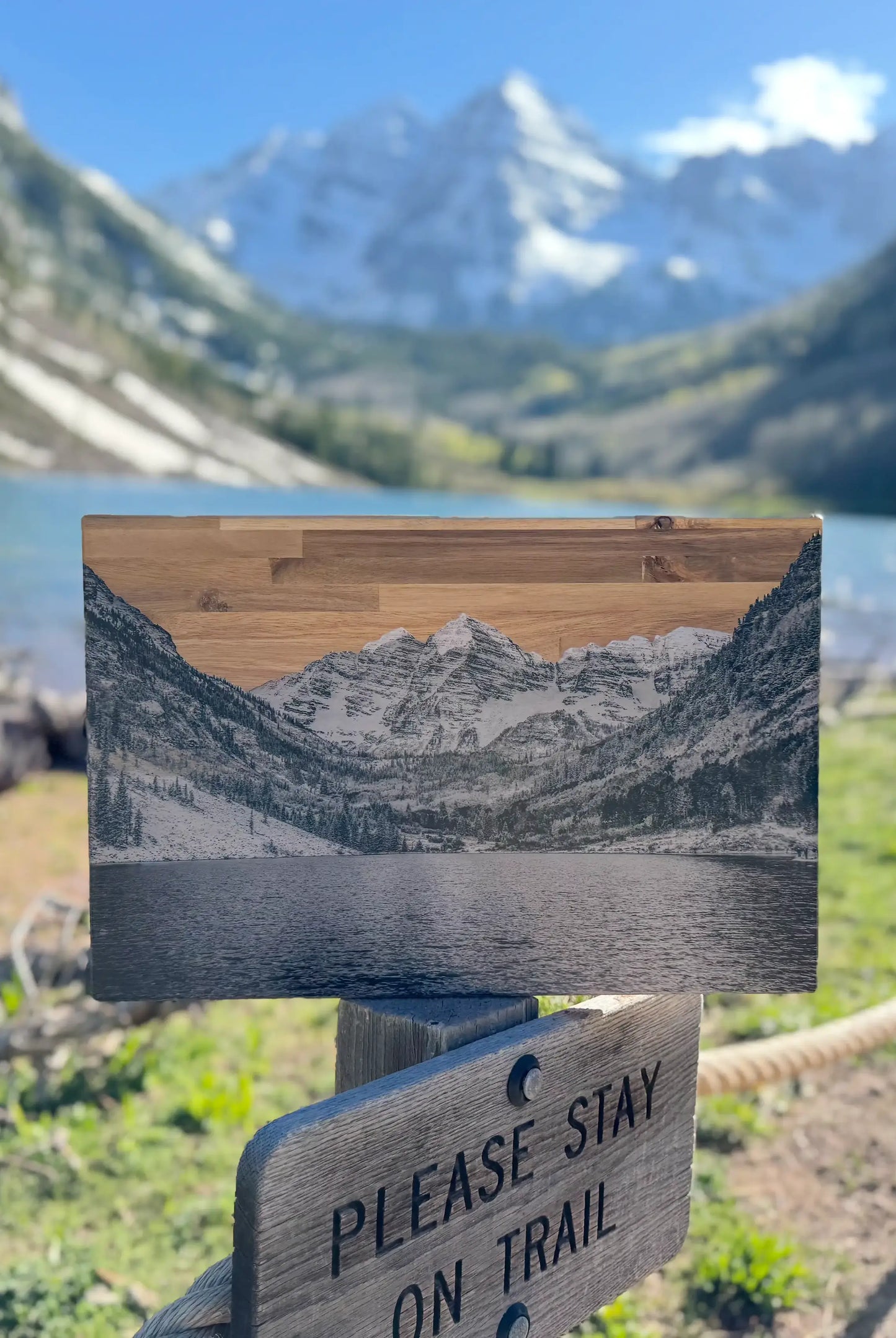 Wooden sign with mountain design in a scenic outdoor setting with lake and mountains. display_on