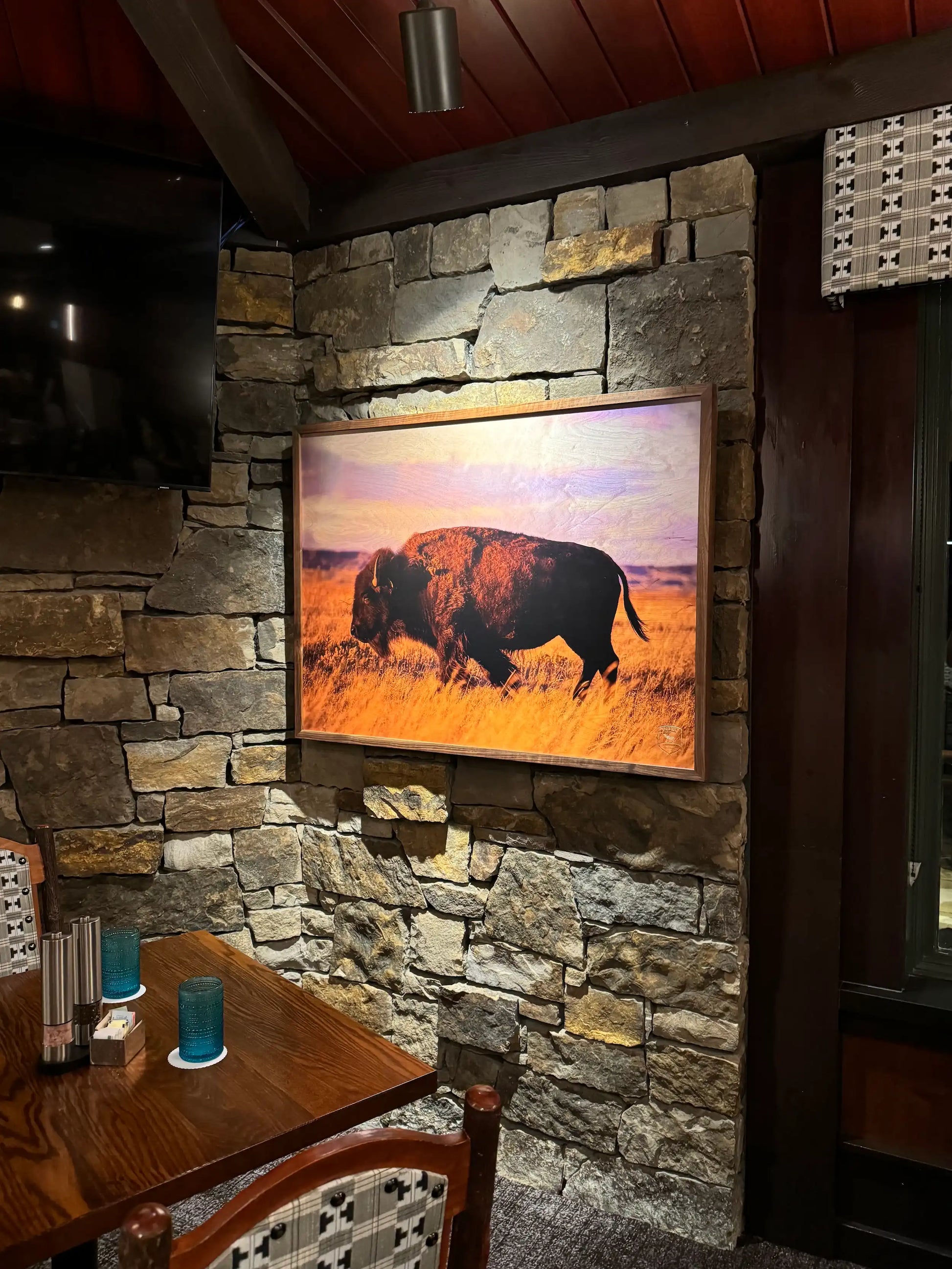 Room interior with stone wall, framed picture of a buffalo, and wooden table.