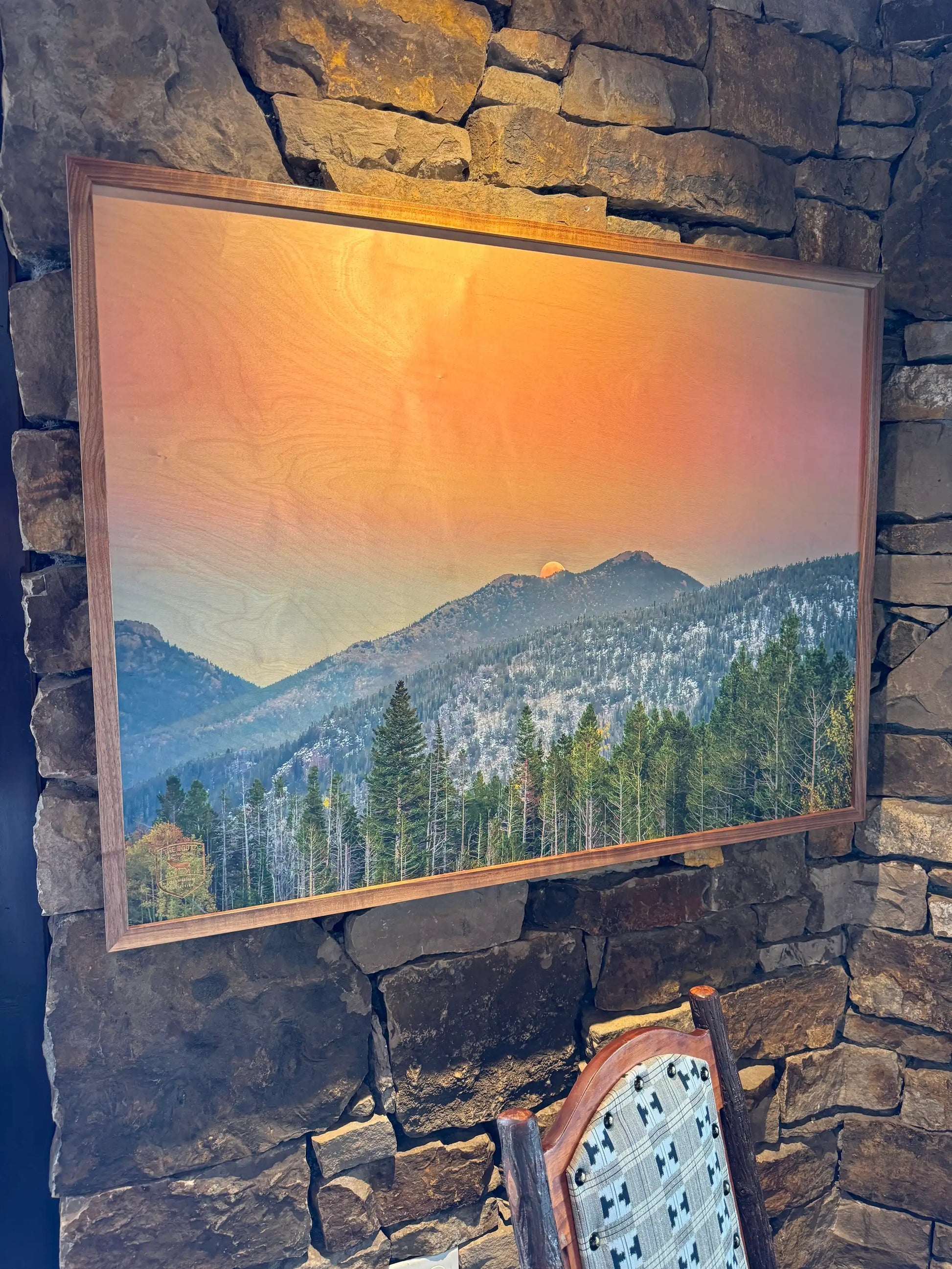 Framed landscape painting of a mountain scene on a stone wall.