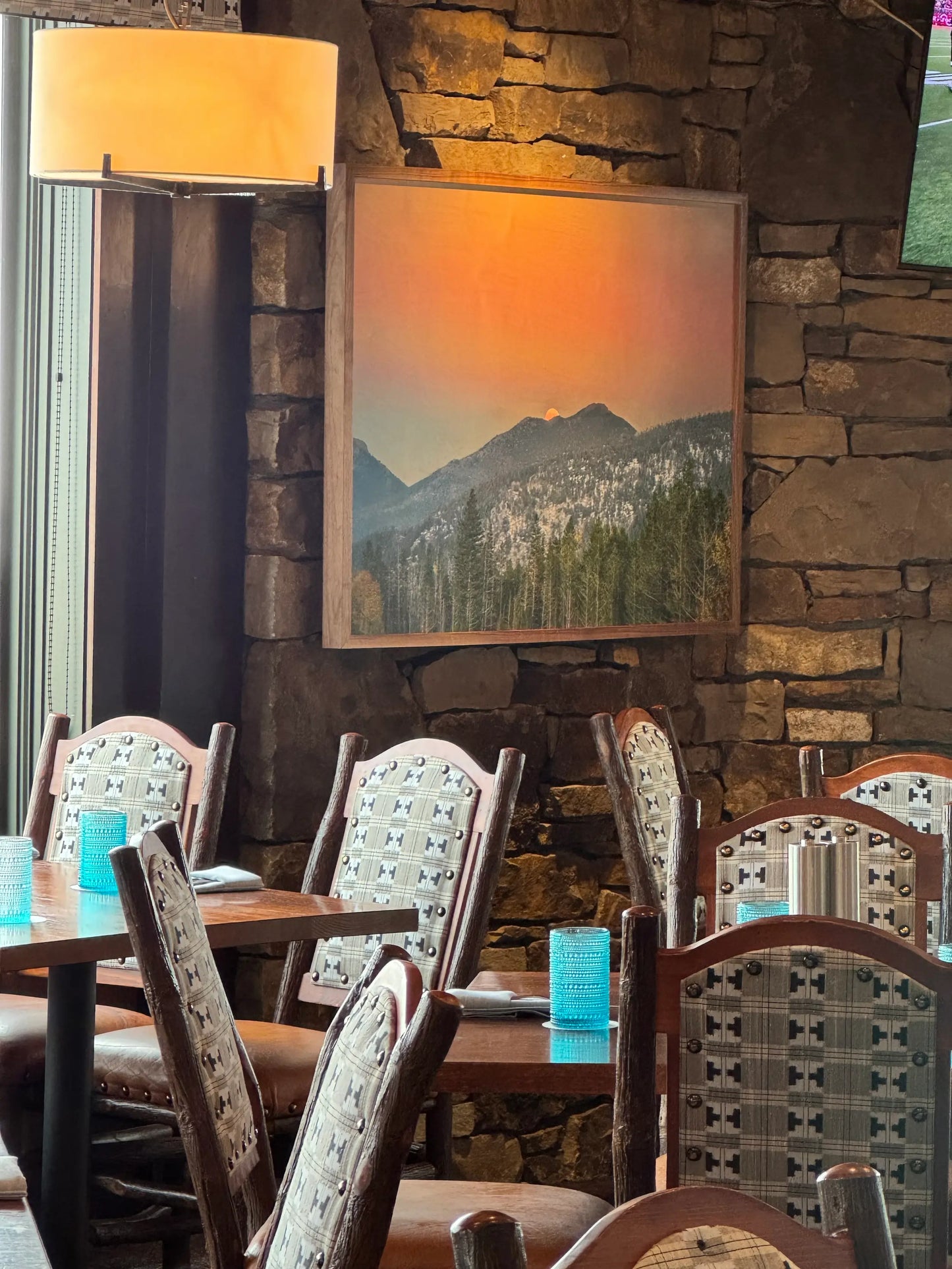 Dining area with wooden tables and chairs, stone wall, and mountain print.