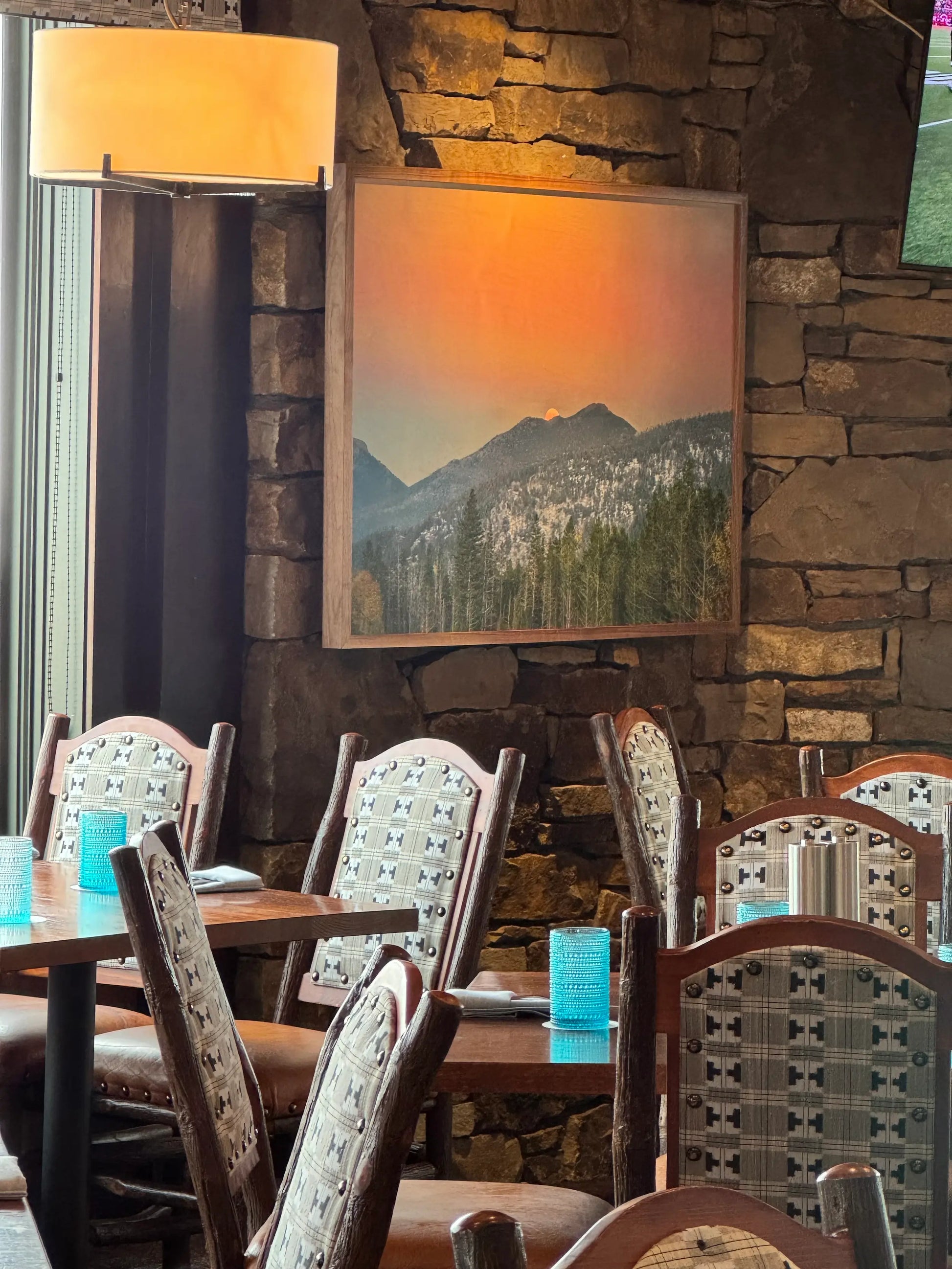 Dining area with wooden tables and chairs, stone wall, and mountain print.