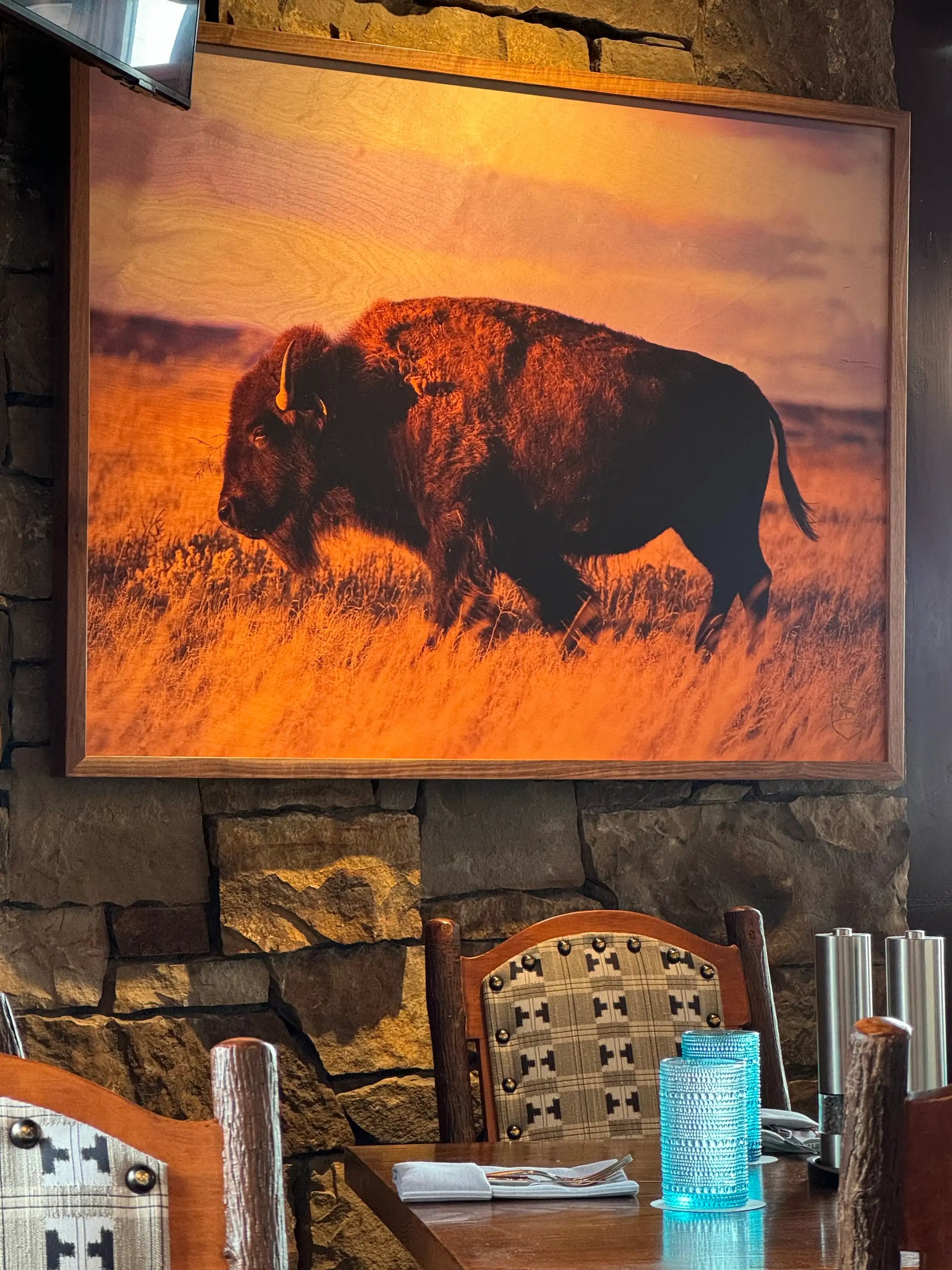 Framed artwork of a bison on a stone wall above a dining table.