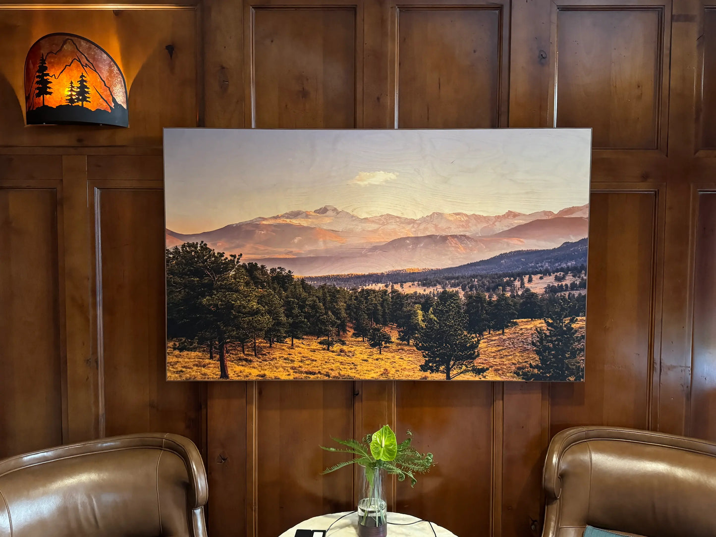 Landscape painting on a wooden wall with two chairs and a small table.