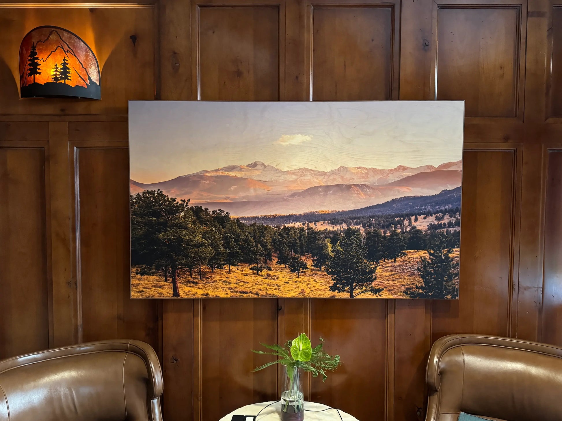 Landscape painting on a wooden wall with two chairs and a small table.