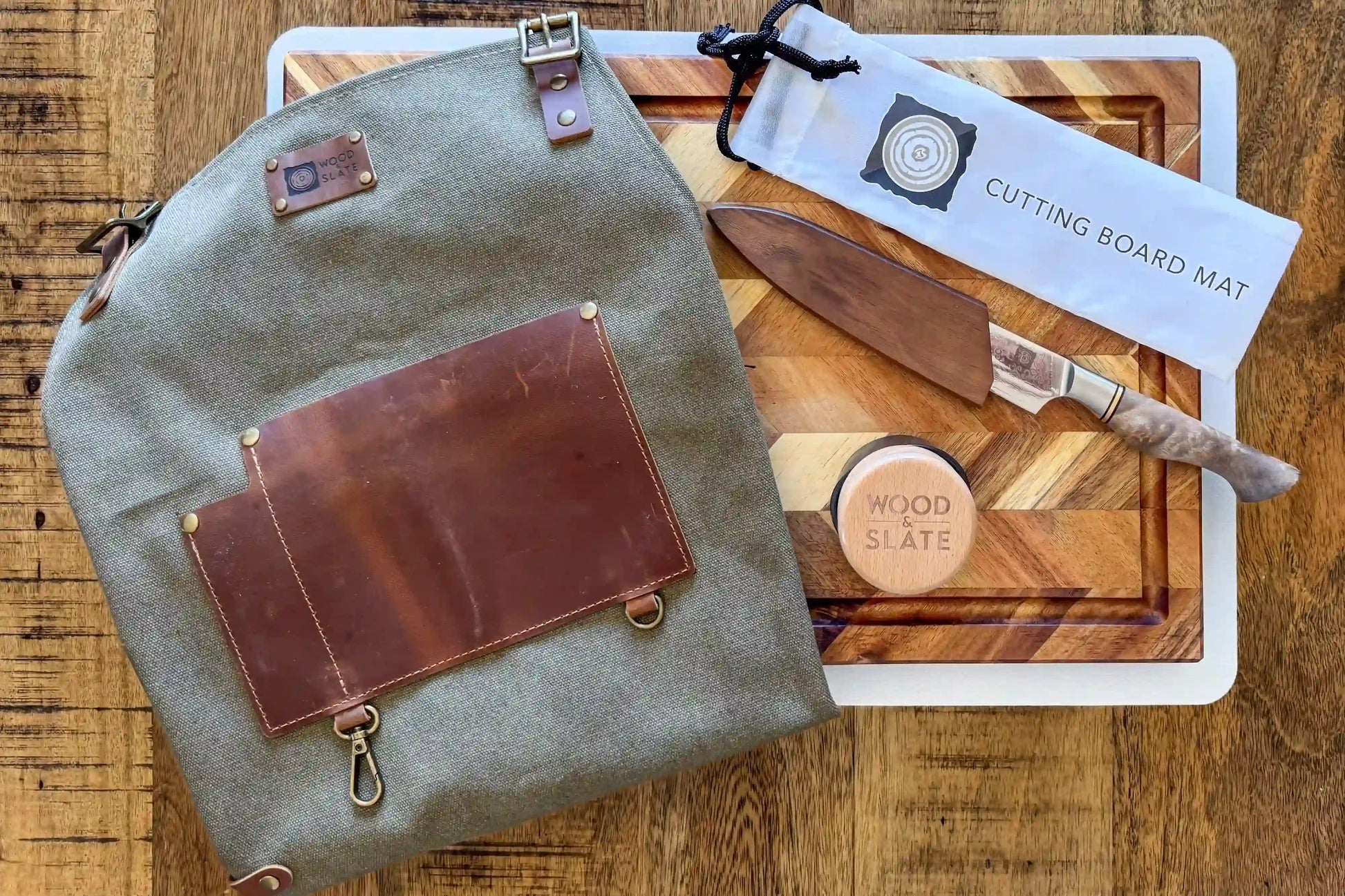 Gray backpack with leather accents on a wooden surface next to a cutting board set.
