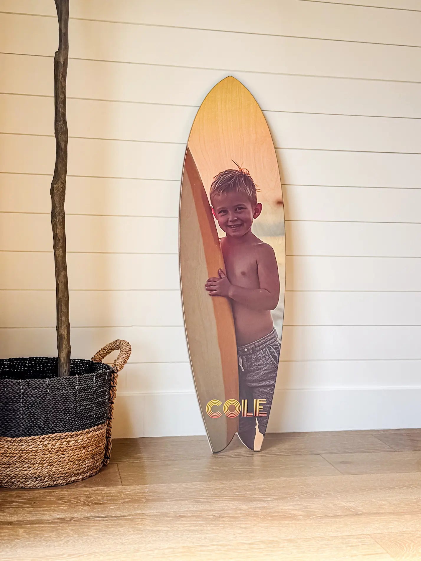 Surfboard with a child's photo on a wooden floor next to a basket. display_on
